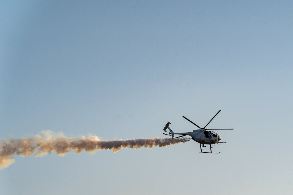 helicopter flying through blue skies while spraying an agricultural treatment