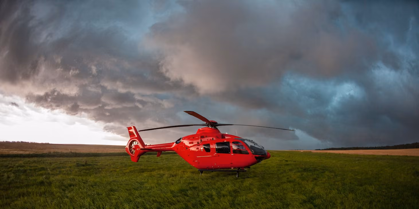 red helicopter resting on a grassy field beneath billowing storm clouds
