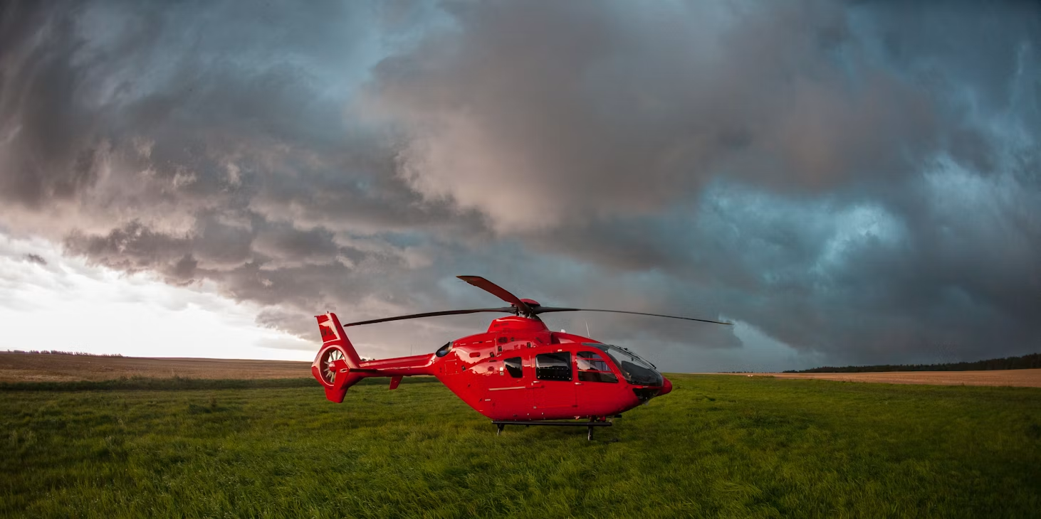 red helicopter resting on a grassy field beneath billowing storm clouds