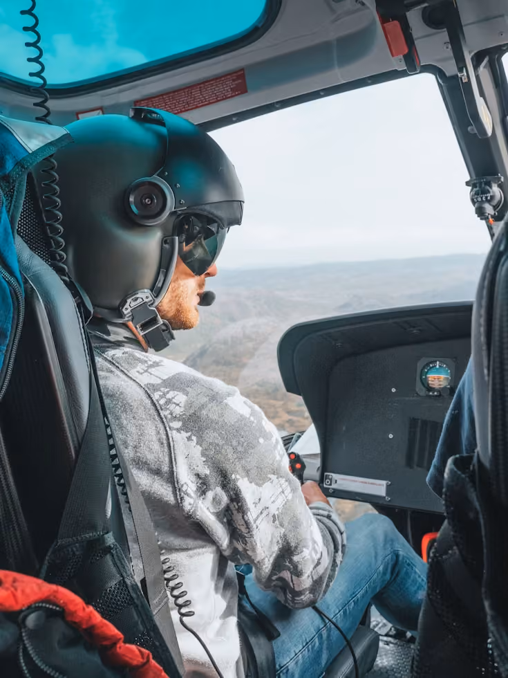 close up view of a helicopter pilot wearing a helmet with a microphone and holding a controller during flight