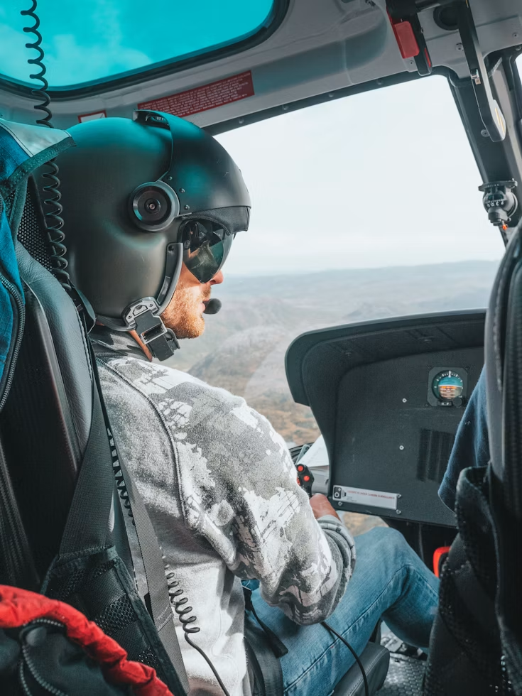 close up view of a helicopter pilot wearing a helmet with a microphone and holding a controller during flight