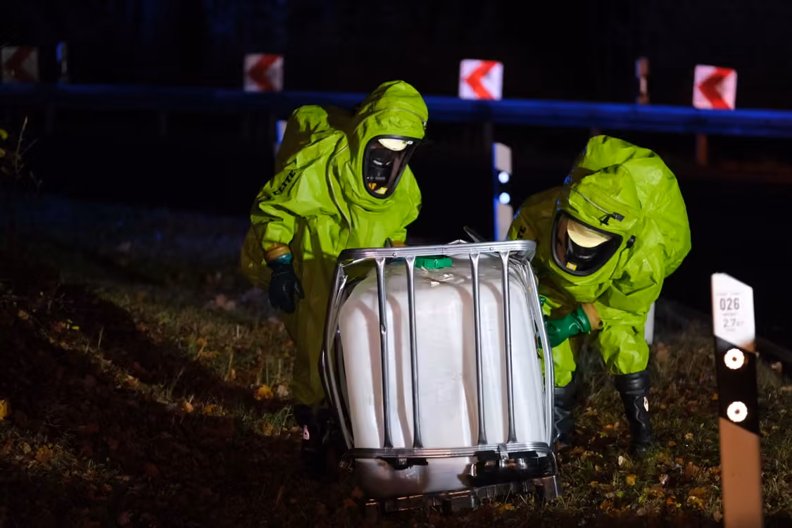 two responders in neon green hazmat suits managing a chemical spill by the roadside at night