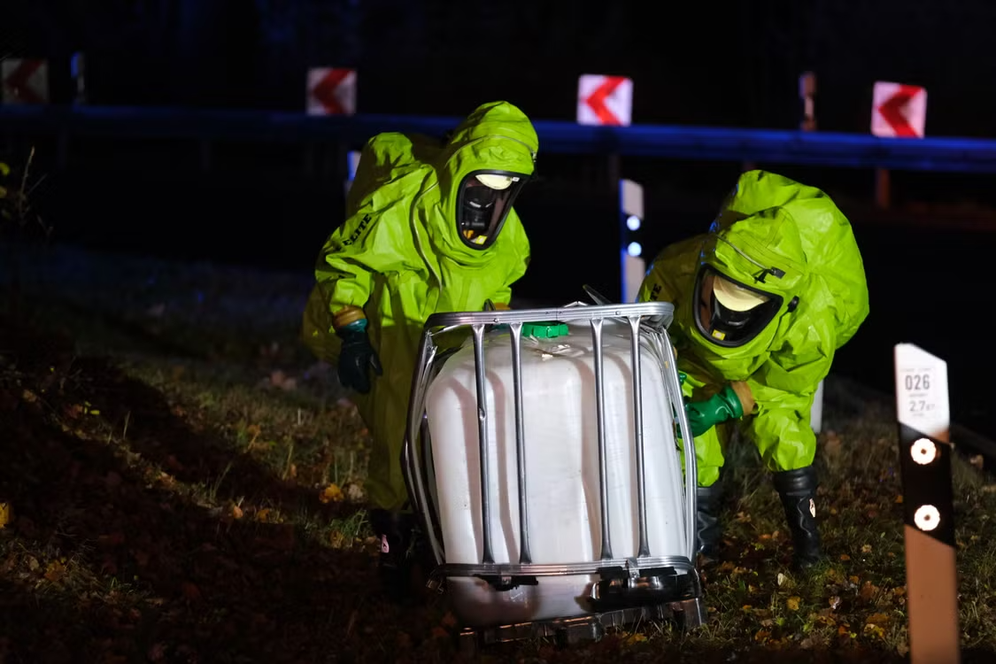 two responders in neon green hazmat suits managing a chemical spill by the roadside at night