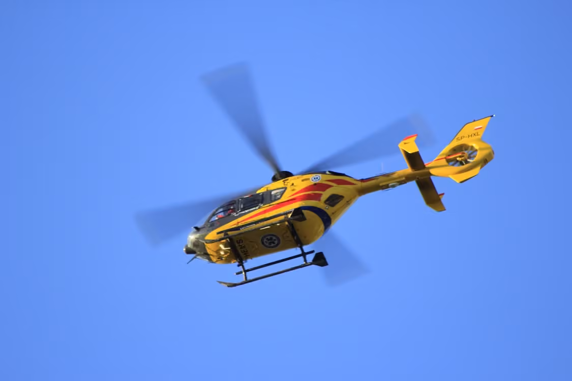 yellow helicopter with red stripes flying through clear blue skies