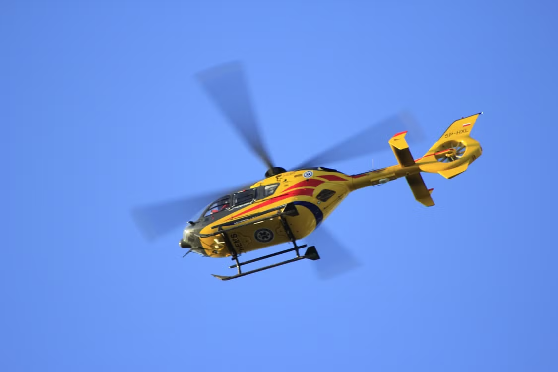 yellow helicopter with red stripes flying through clear blue skies