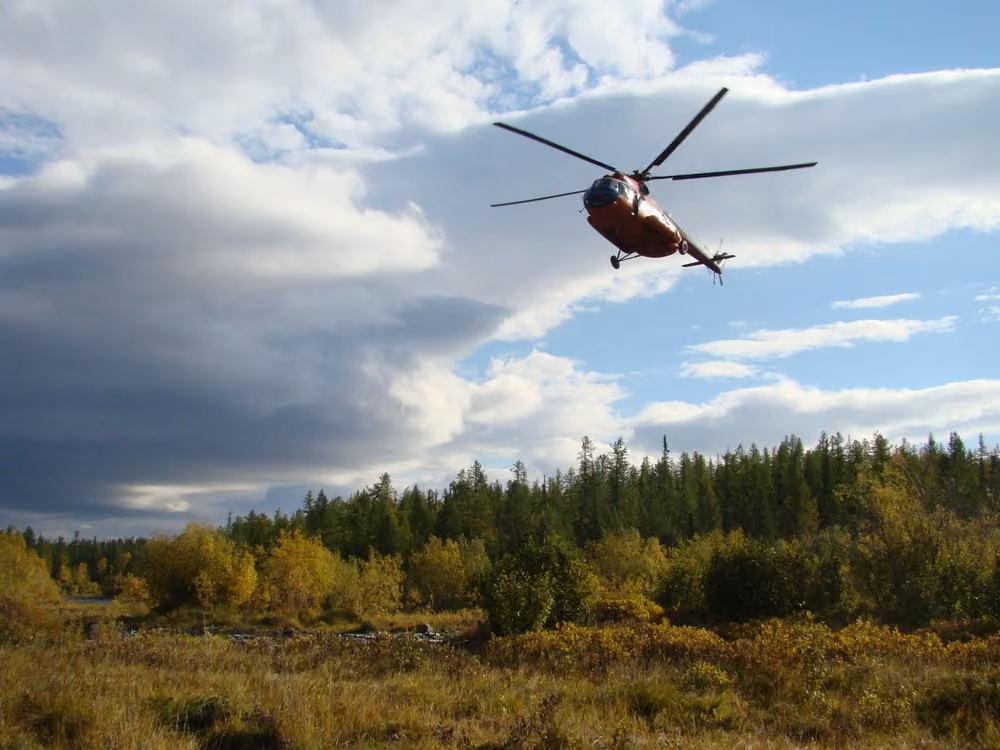 red and white helicopter soaring above a forest landscape under a partly cloudy sky