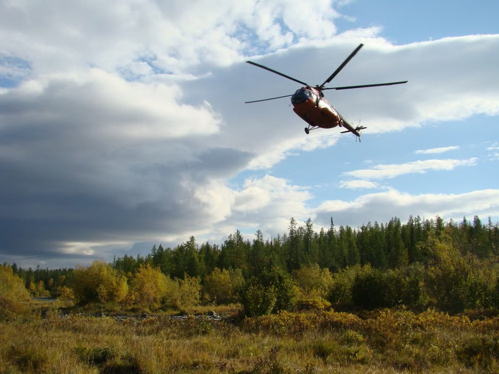 red and white helicopter soaring above a forest landscape under a partly cloudy sky