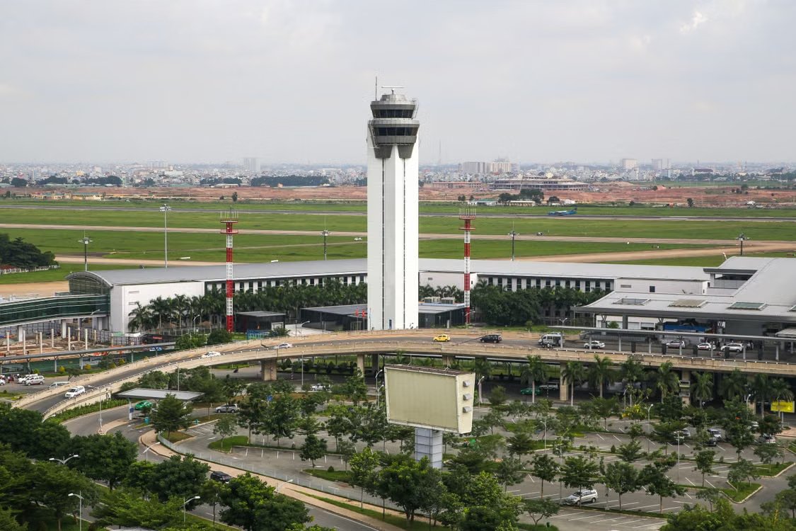 aerial view of a busy airport with a prominent control tower surrounded by roads and greenery