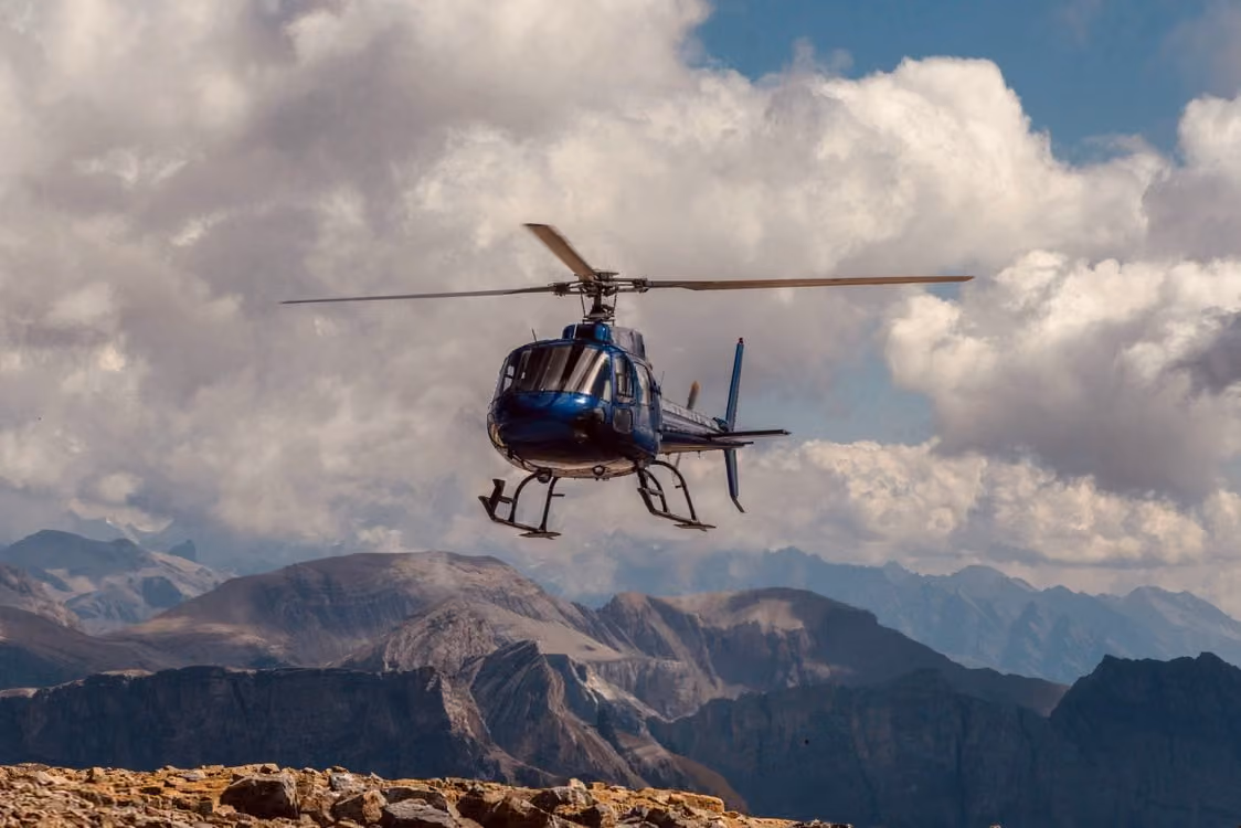blue helicopter flying over breathtaking mountain landscape with dramatic clouds in the sky