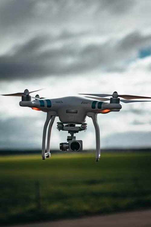 white drone with integrated camera flying low over a green field under a dramatic cloudy sky