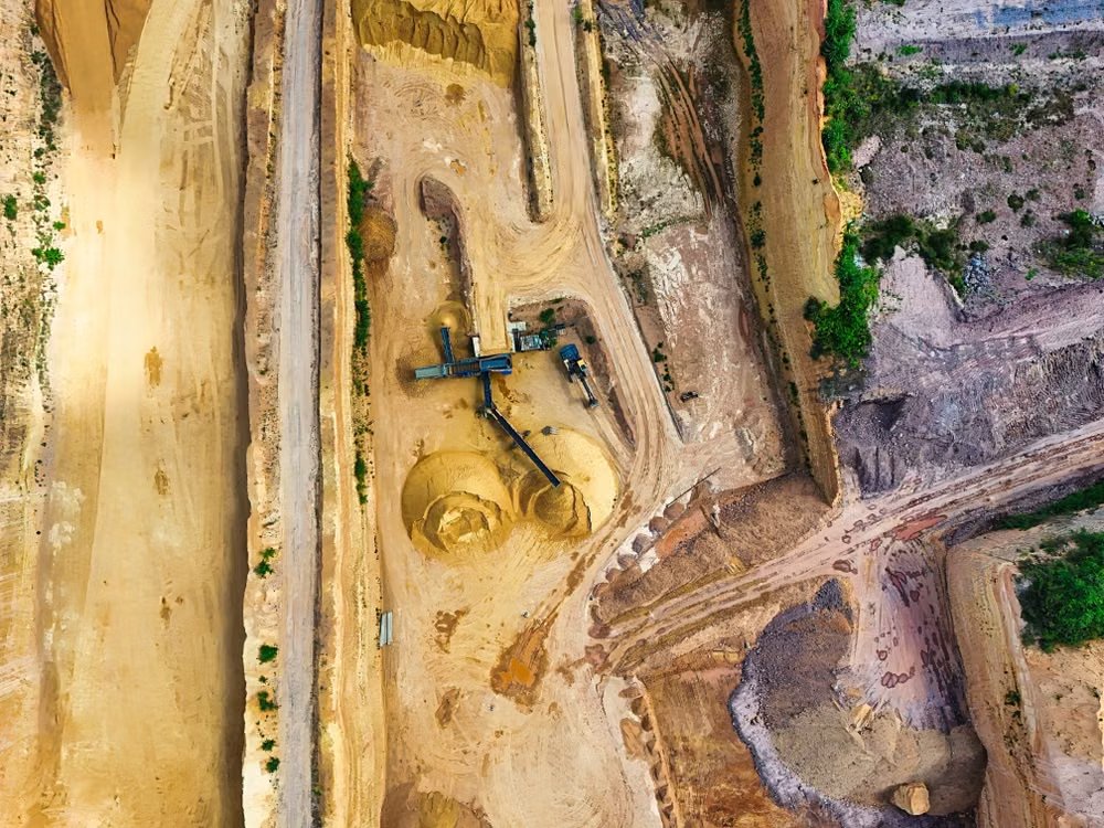 aerial shot of an open-pit mine with machinery and pathways visible, surrounded by landscape