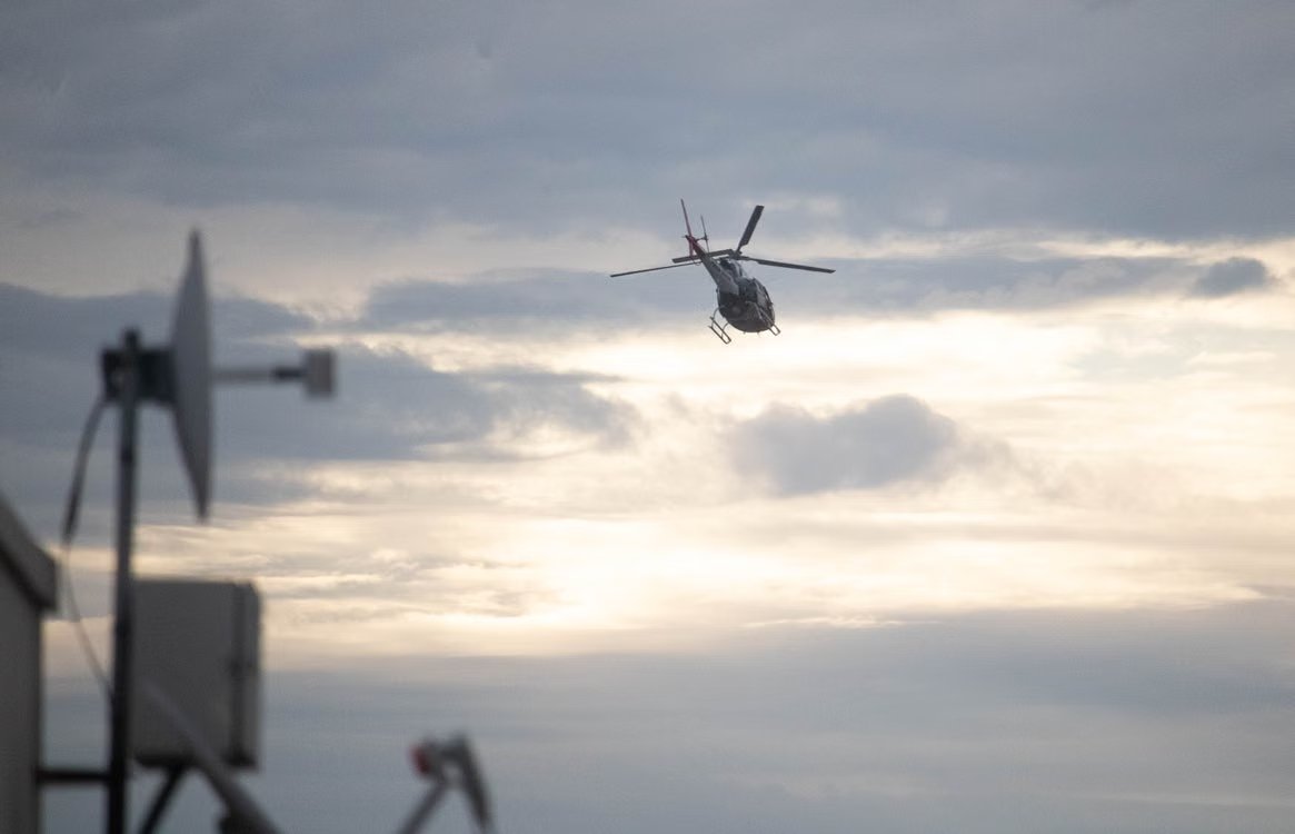 helicopter flies in the cloudy evening sky with urban communication structures in the foreground