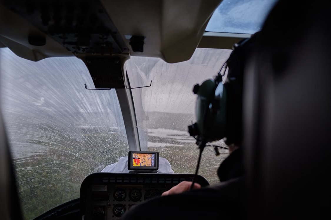 inside view of a helicopter cockpit and navigation system as the pilot flies over a flooded landscape during rain