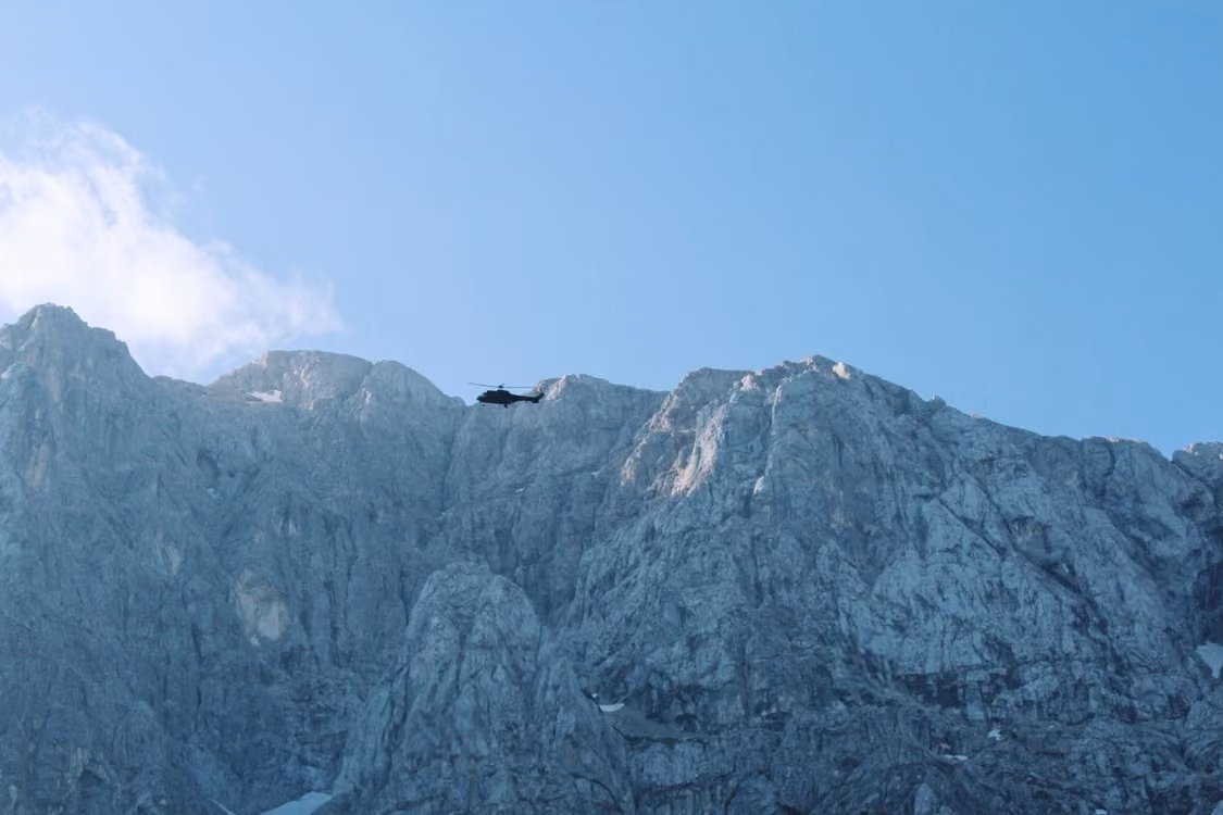 silhouette of a helicopter soaring against a backdrop of rocky mountains under a blue sky