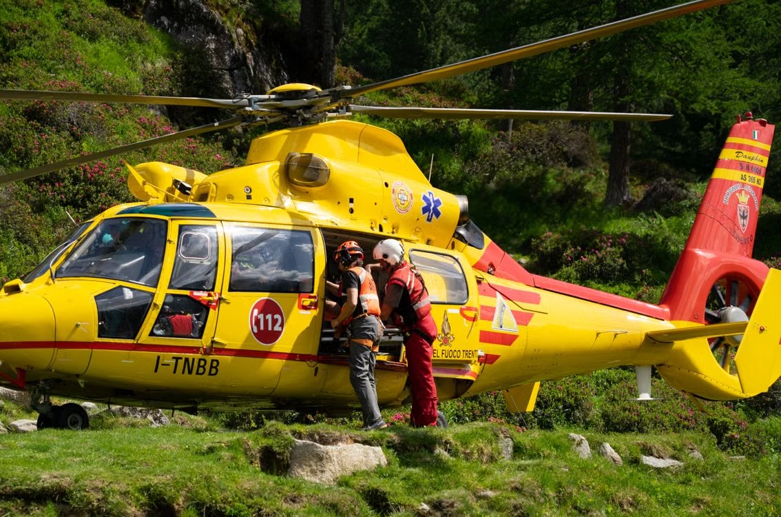 emergency rescue team entering a red and yellow rescue helicopter in a mountainous rural area