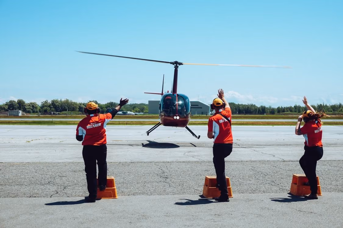 ground crew in matching red shirts and orange hats directing a helicopter landing under blue skies
