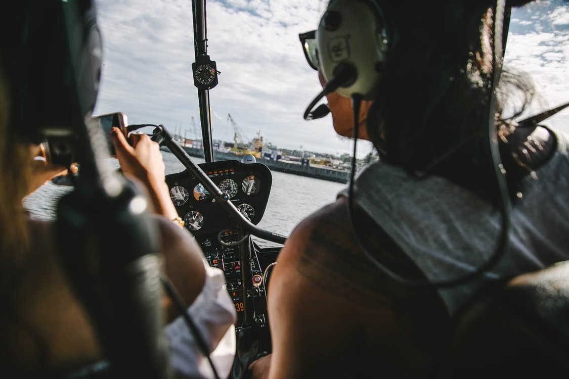 view from a helicopter cockpit featuring pilots wearing headphones flying over the coast during daytime