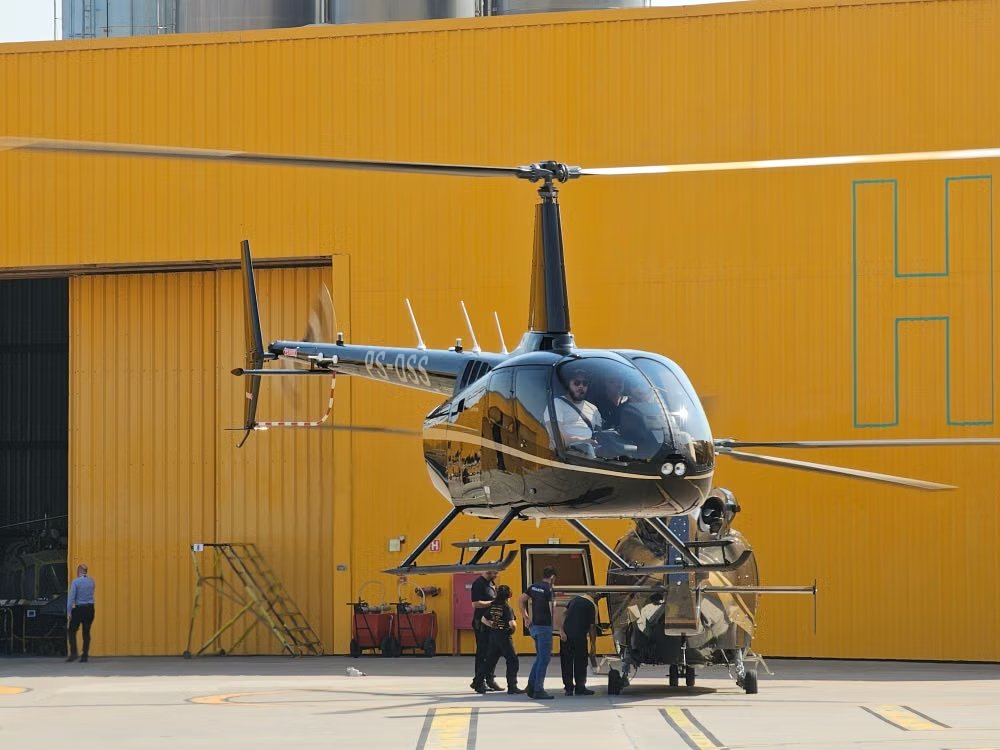 black helicopter stationed in front of a bright orange aircraft hangar with ground personnel doing final inspections