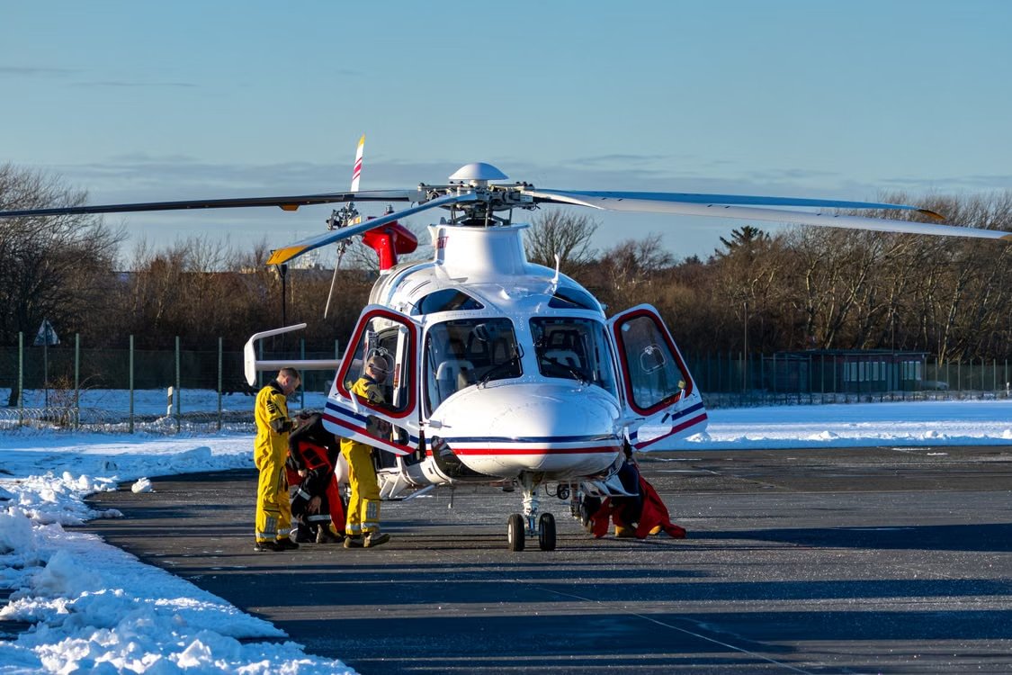 emergency personnel in yellow gear standing outside a white helicopter on a snowy runway during a winter operation