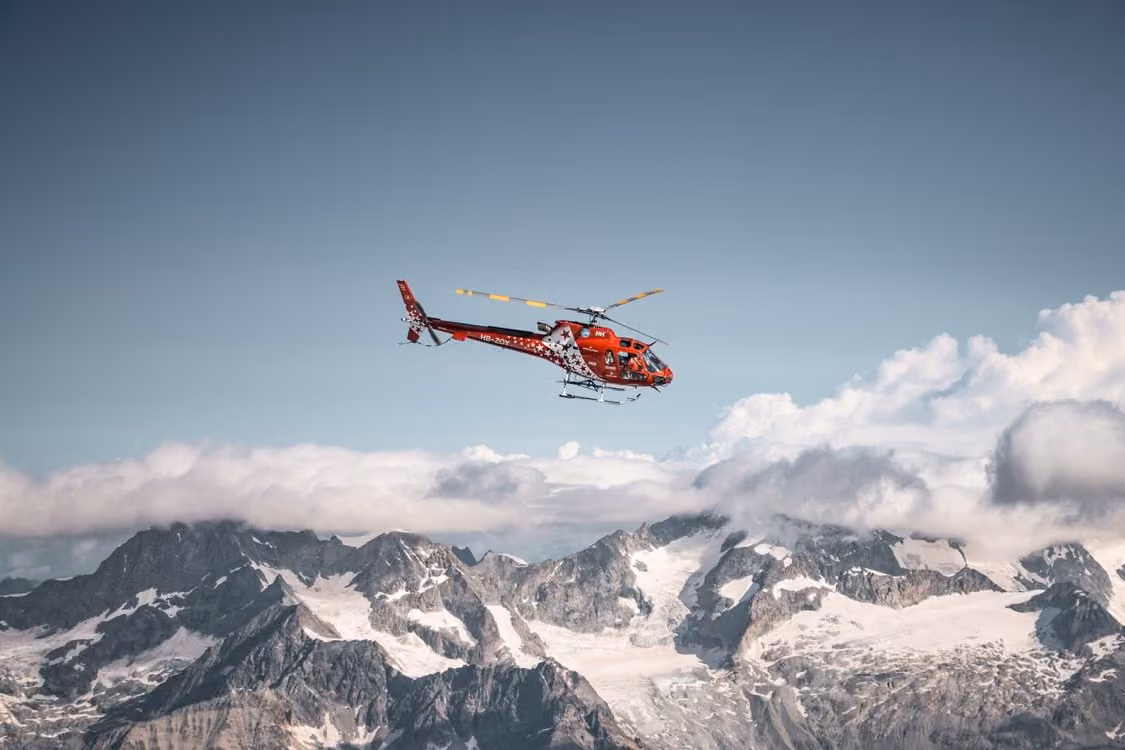 red and white helicopter flies over the snowy peaks of the Swiss Alps