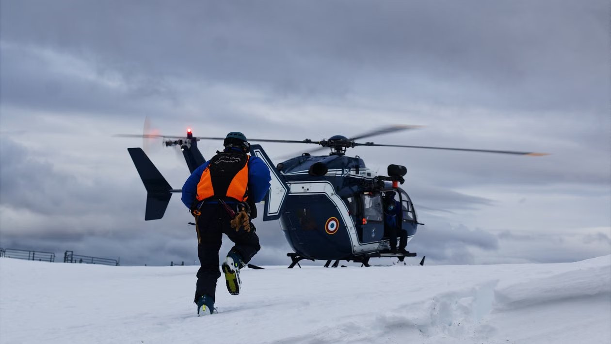 emergency response rescue worker approaches a black and white helicopter sitting on snowy field under gray skies