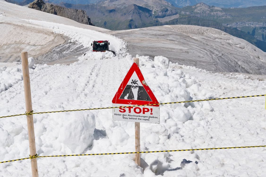 red, black, and white avalanche warning sign on a snowy trail in the Swiss Alps with panoramic mountain views