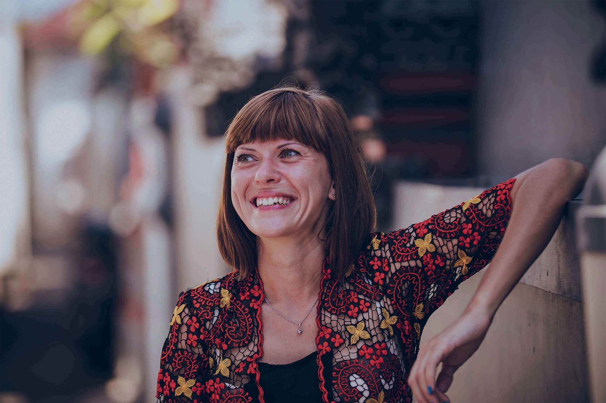 A smiling woman with a fringe leaning on a wall outdoors