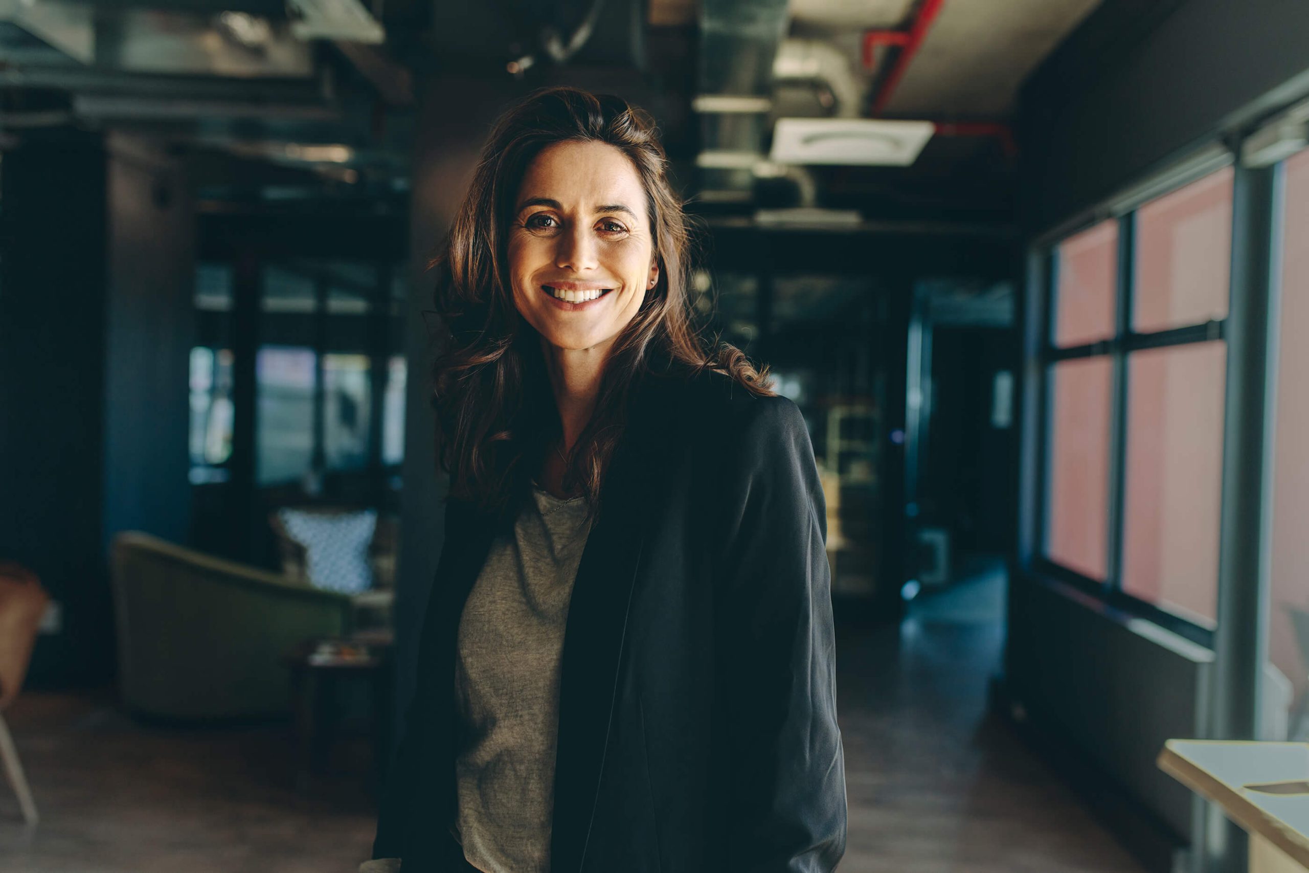 A smiling woman in a blazer standing in an open-plan office