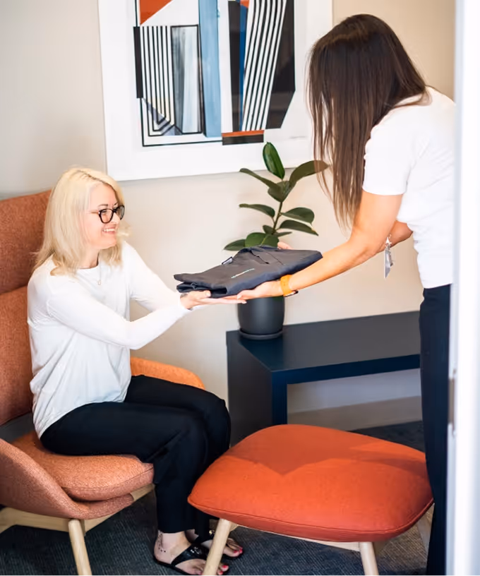A staff member handing folded scrubs to a seated patient