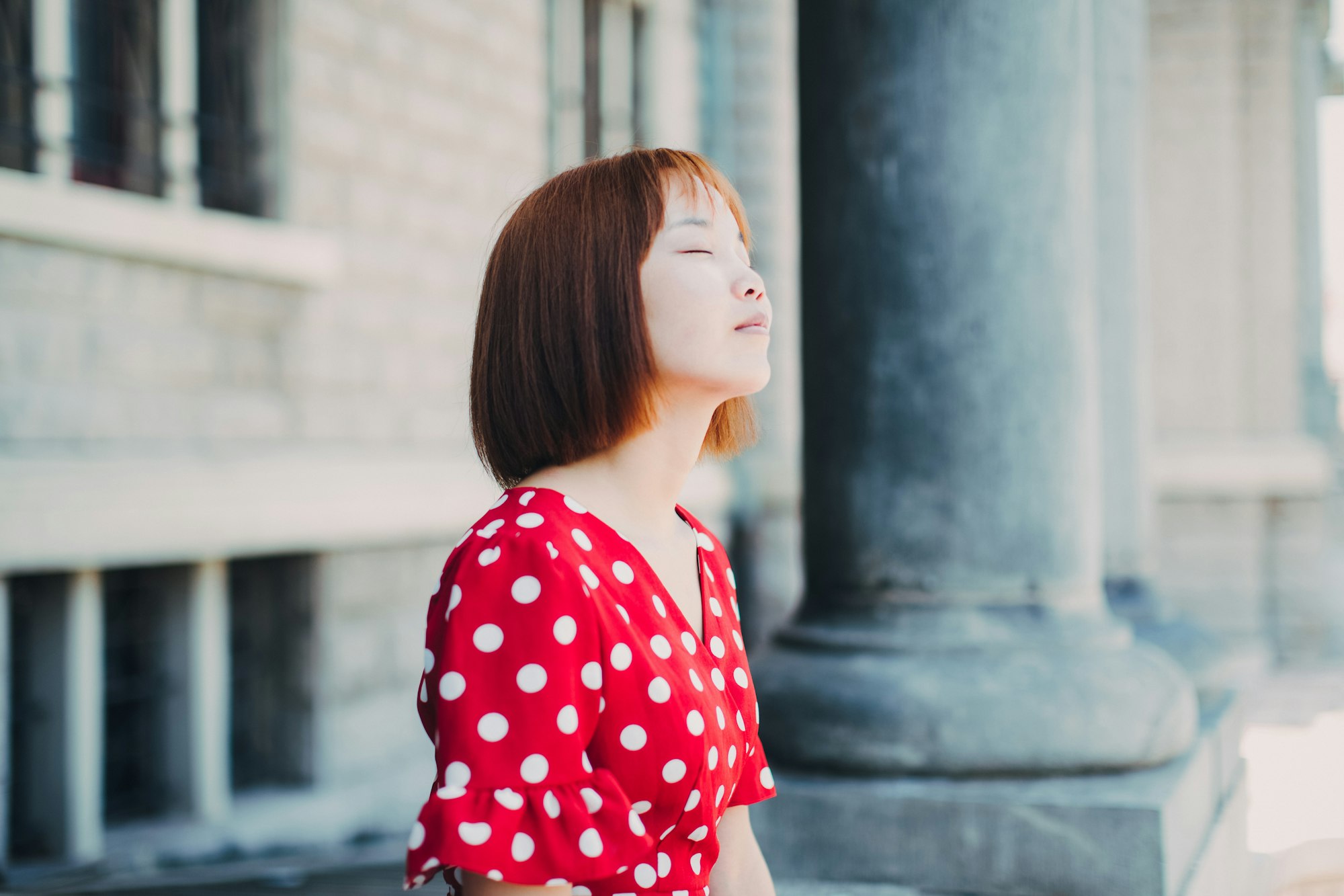 Woman sitting outdoors in daylight with her eyes closed, looking calm and relaxed
