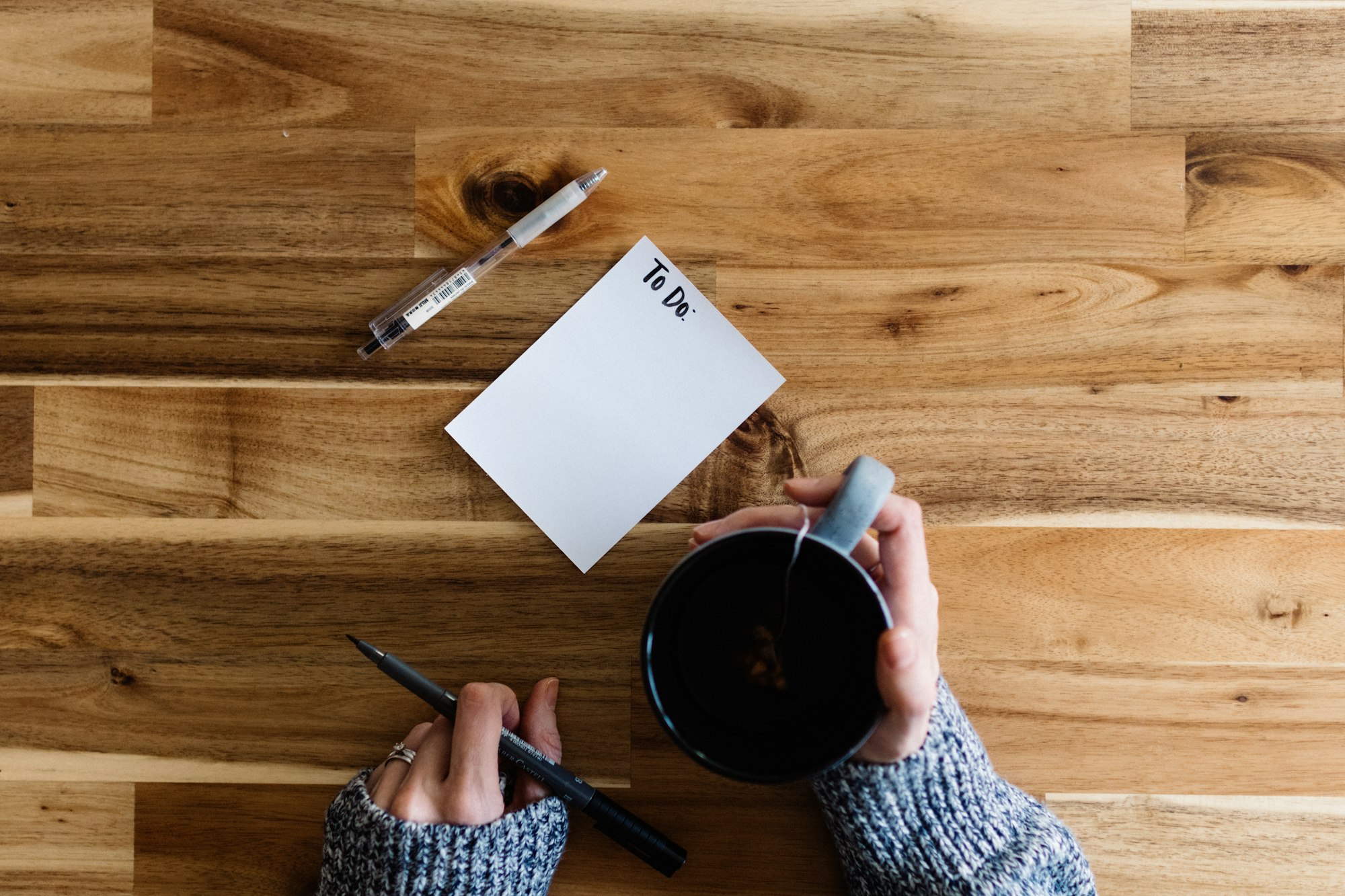 Hands holding a pen beside a blank To Do note and a cup of coffee, ready to write thoughts down