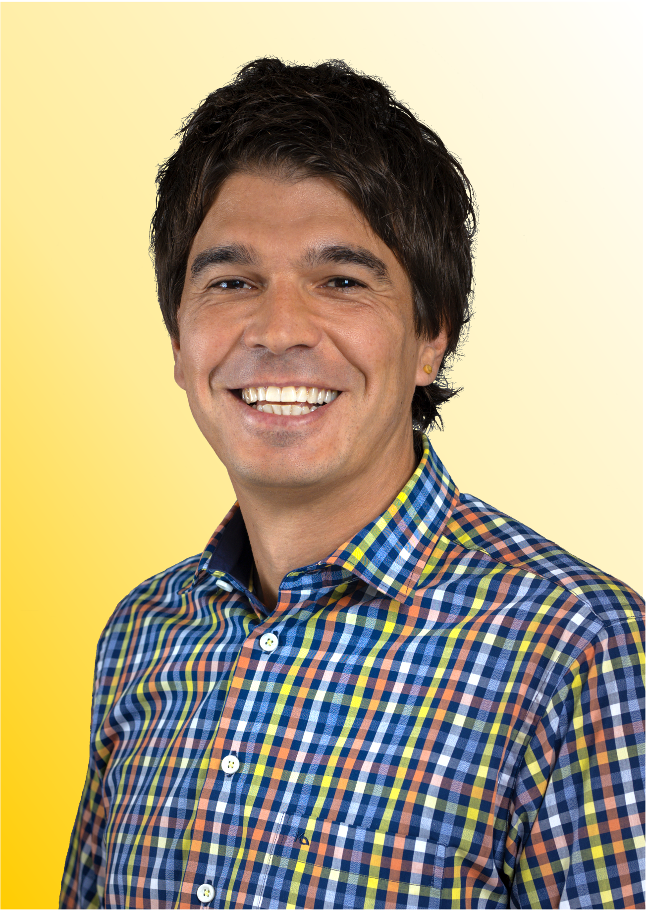 Smiling man with dark hair wearing a colorful checked shirt against a yellow gradient background.