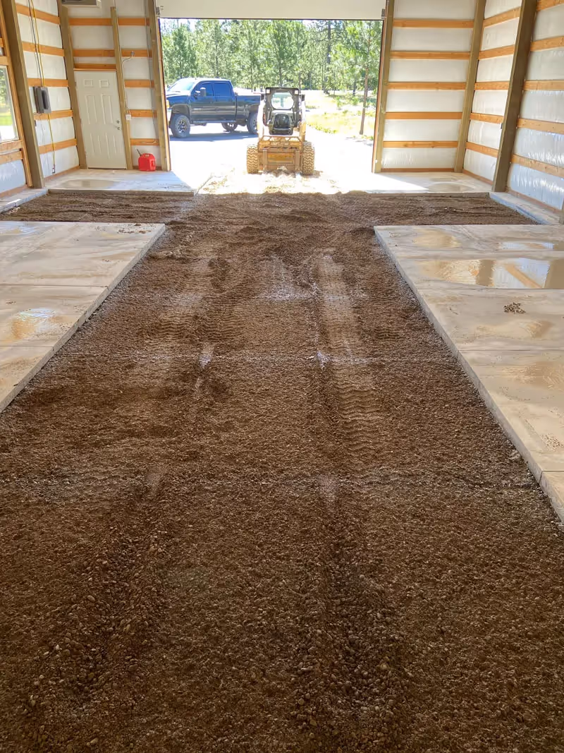 Tilled soil inside a barn with skid steer and truck outside