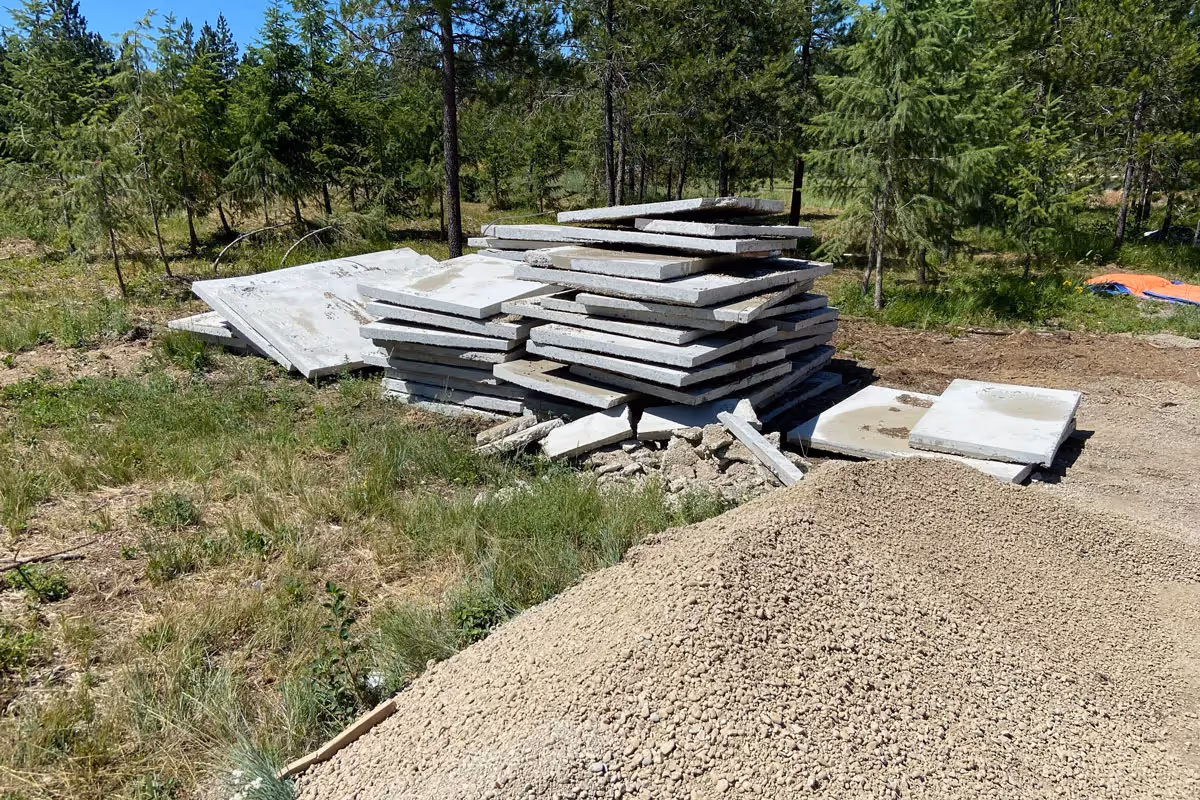 Concrete slabs stacked in a forested construction site with gravel pile