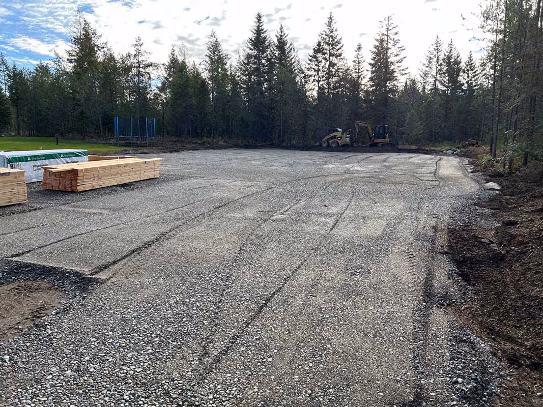 Construction site with gravel lot, lumber, and excavator in forested area