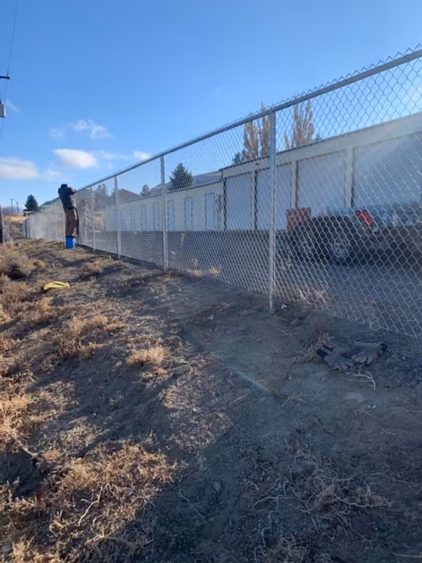 Person standing near chain-link fence on dry, barren ground with blue sky