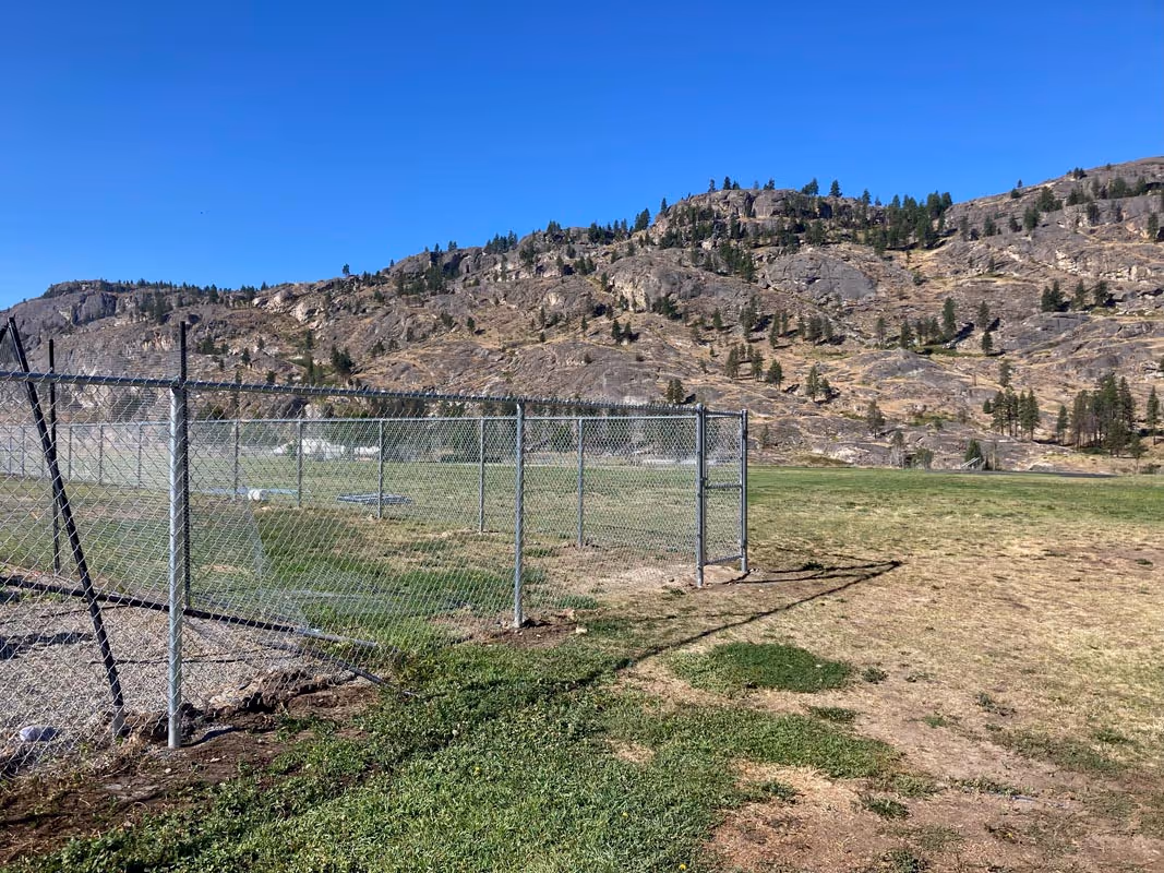 Chain-link fence enclosure on grassy field with rocky mountain backdrop