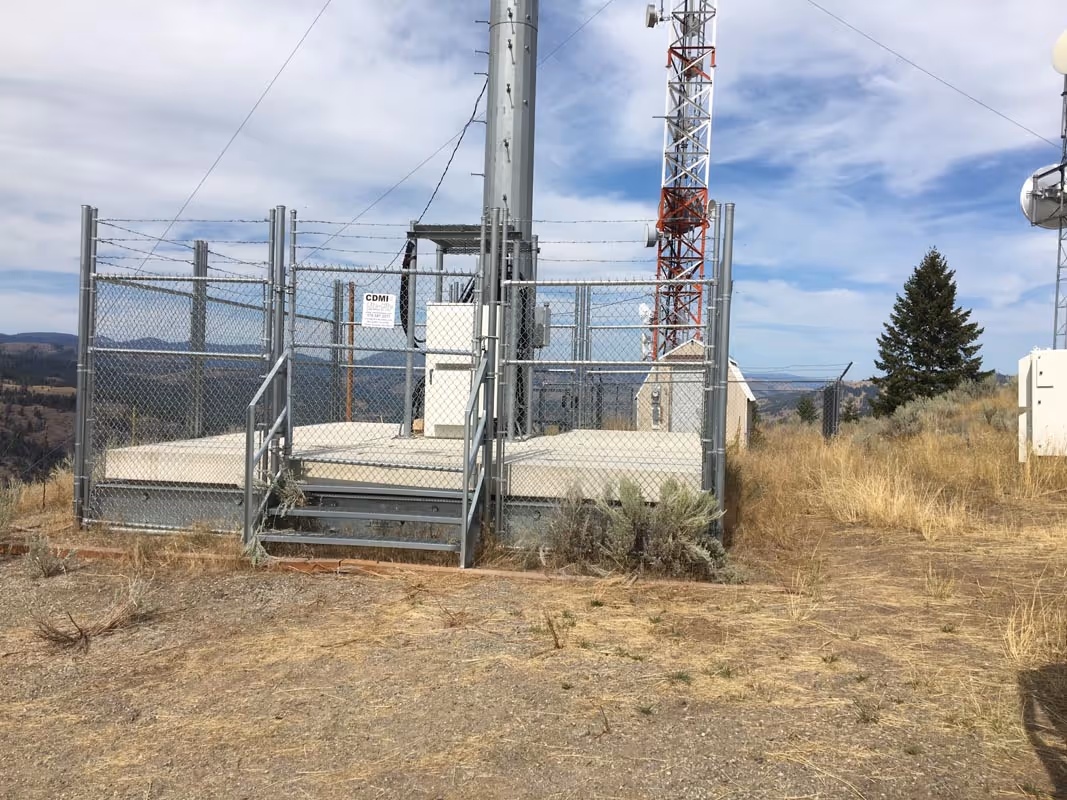 Fenced communication tower with metal structures in dry landscape