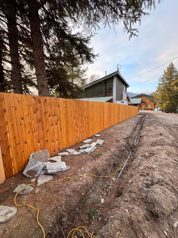 Wooden fence and landscaping with rocks and yellow cable near trees