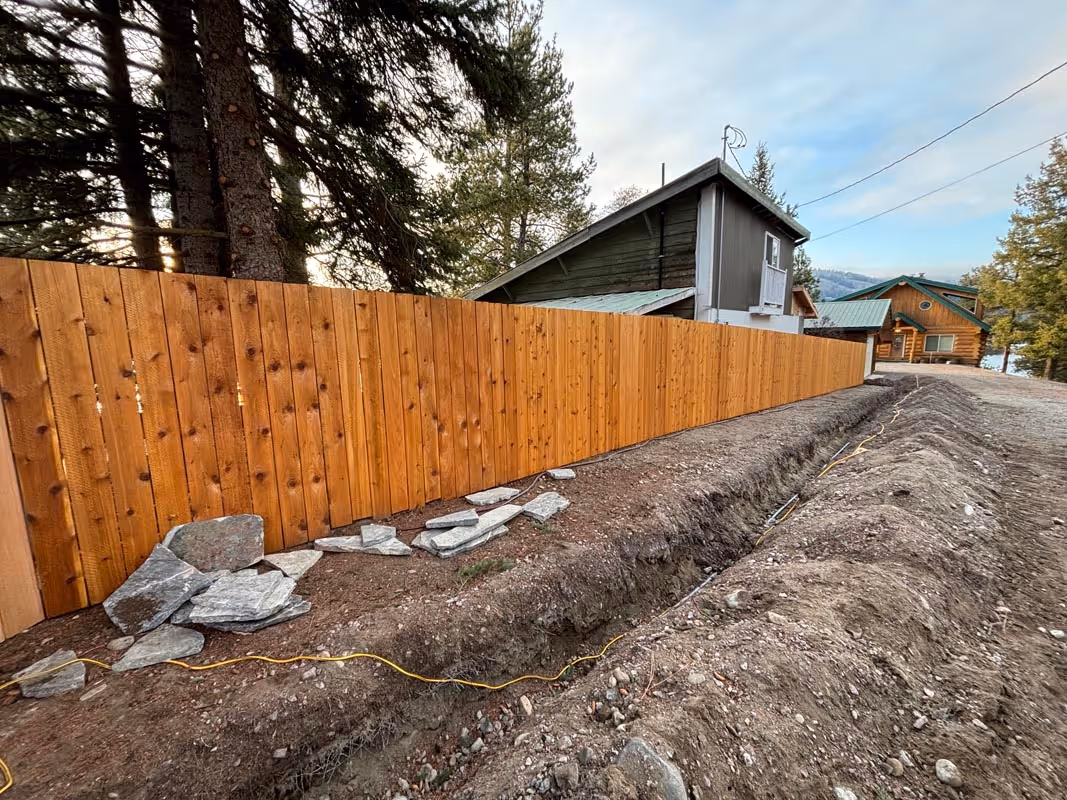 Wooden fence with trench and stones, cabins in background among trees