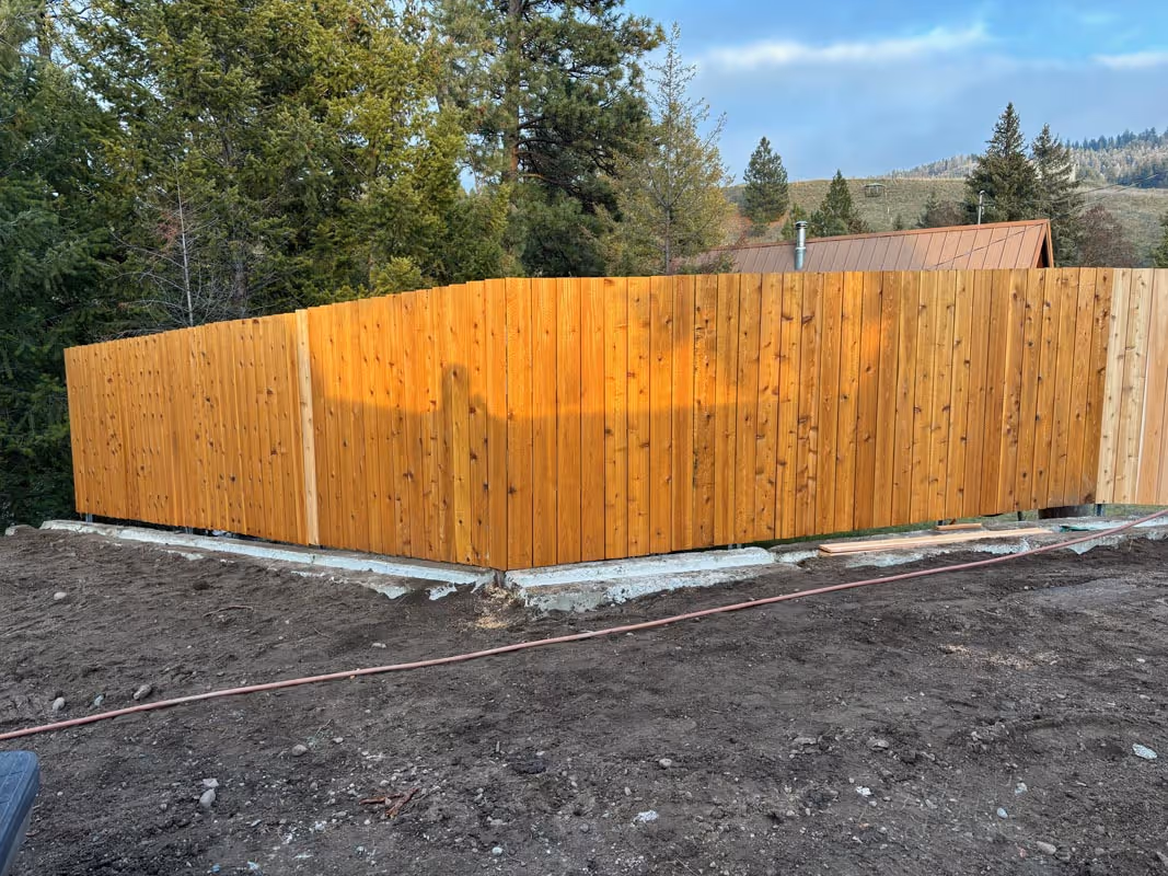 Wooden fence with golden hue on concrete foundation, surrounded by trees