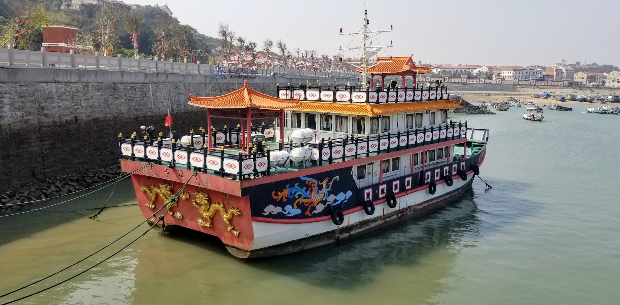 A painted ferry at the harbor, with orange tiled roofs and dragon decoration