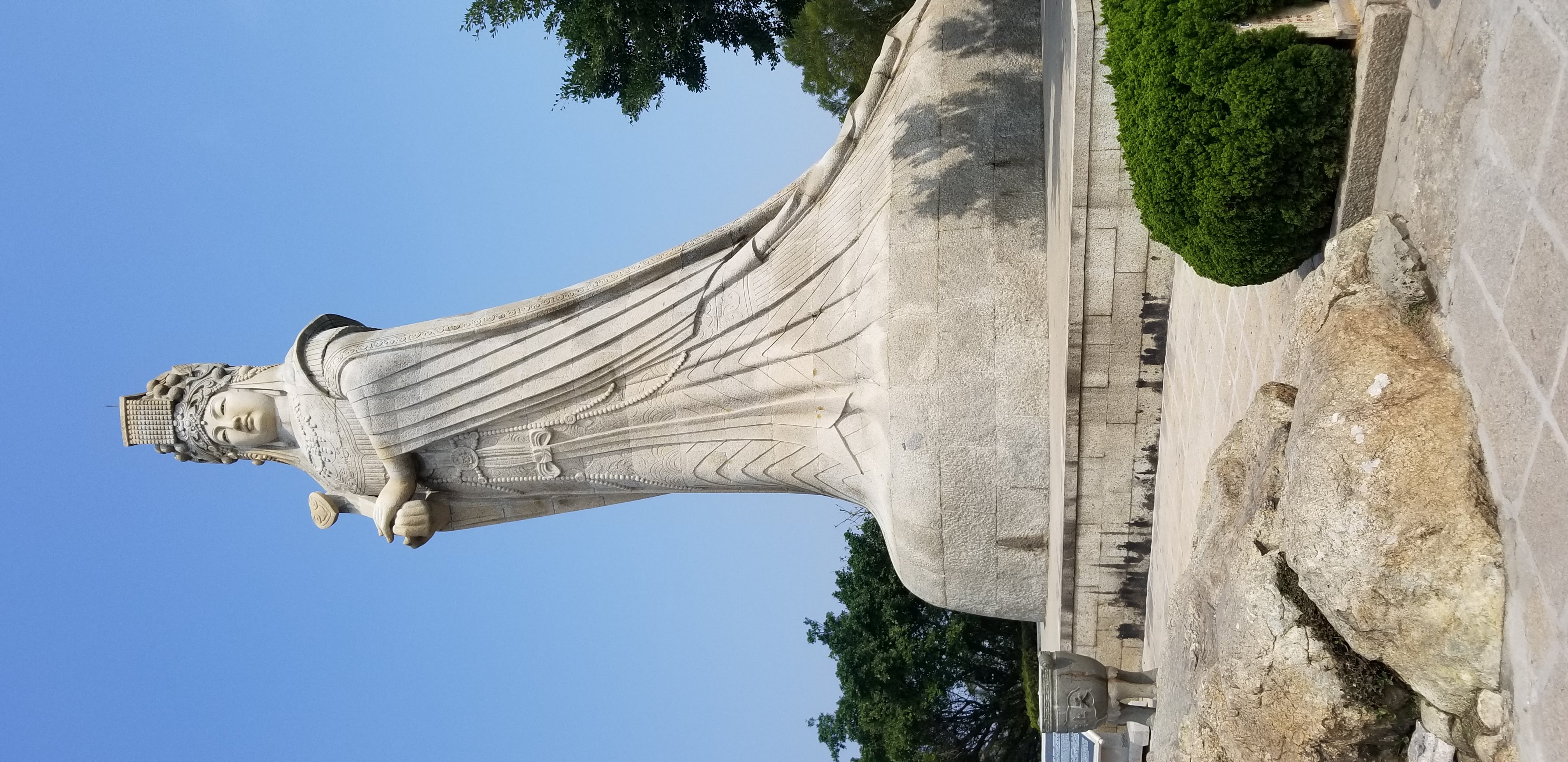 A tall outdoor stone statue of Mazu against a blue sky