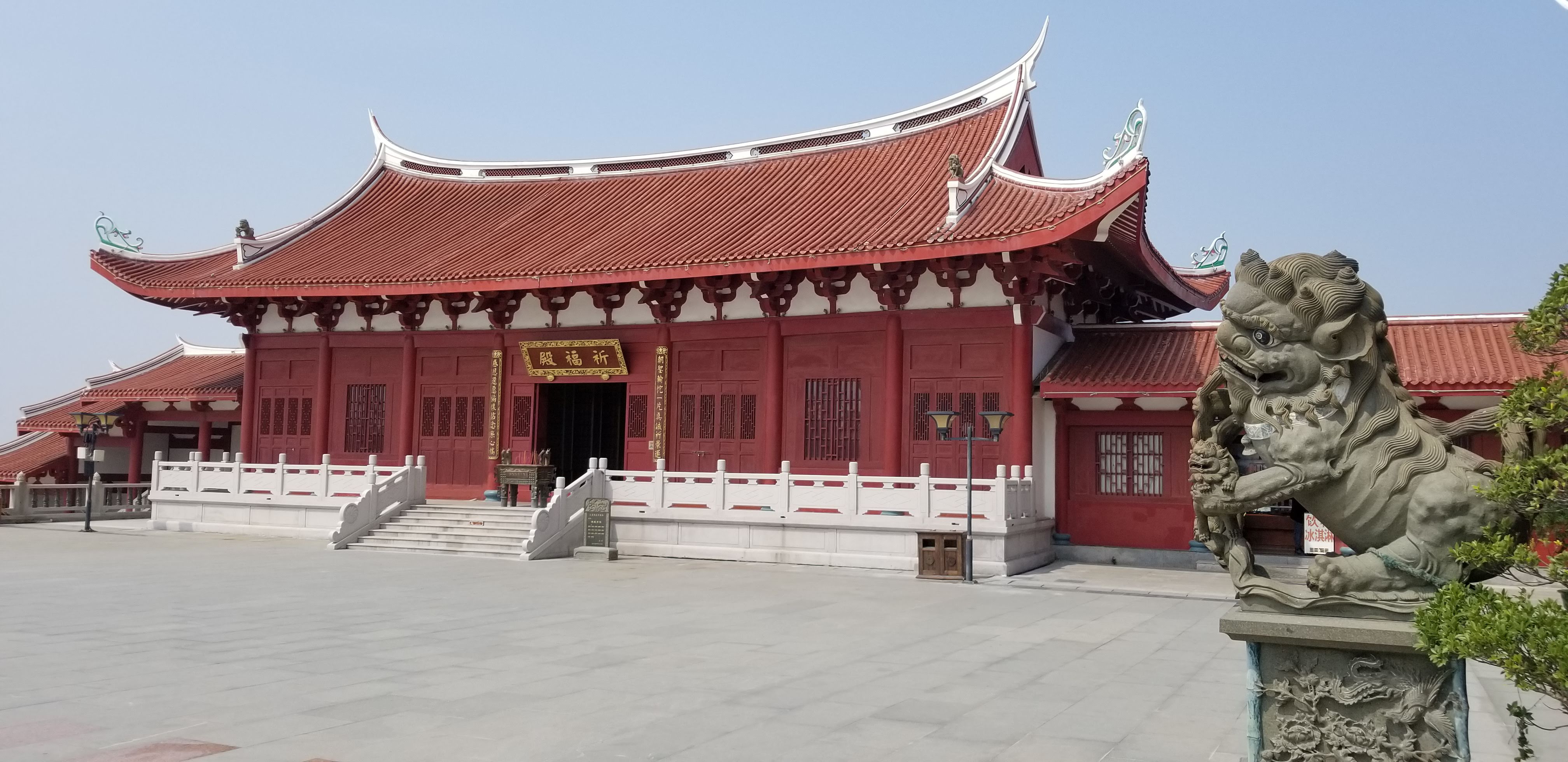 A stone guardian lion beside a red temple hall