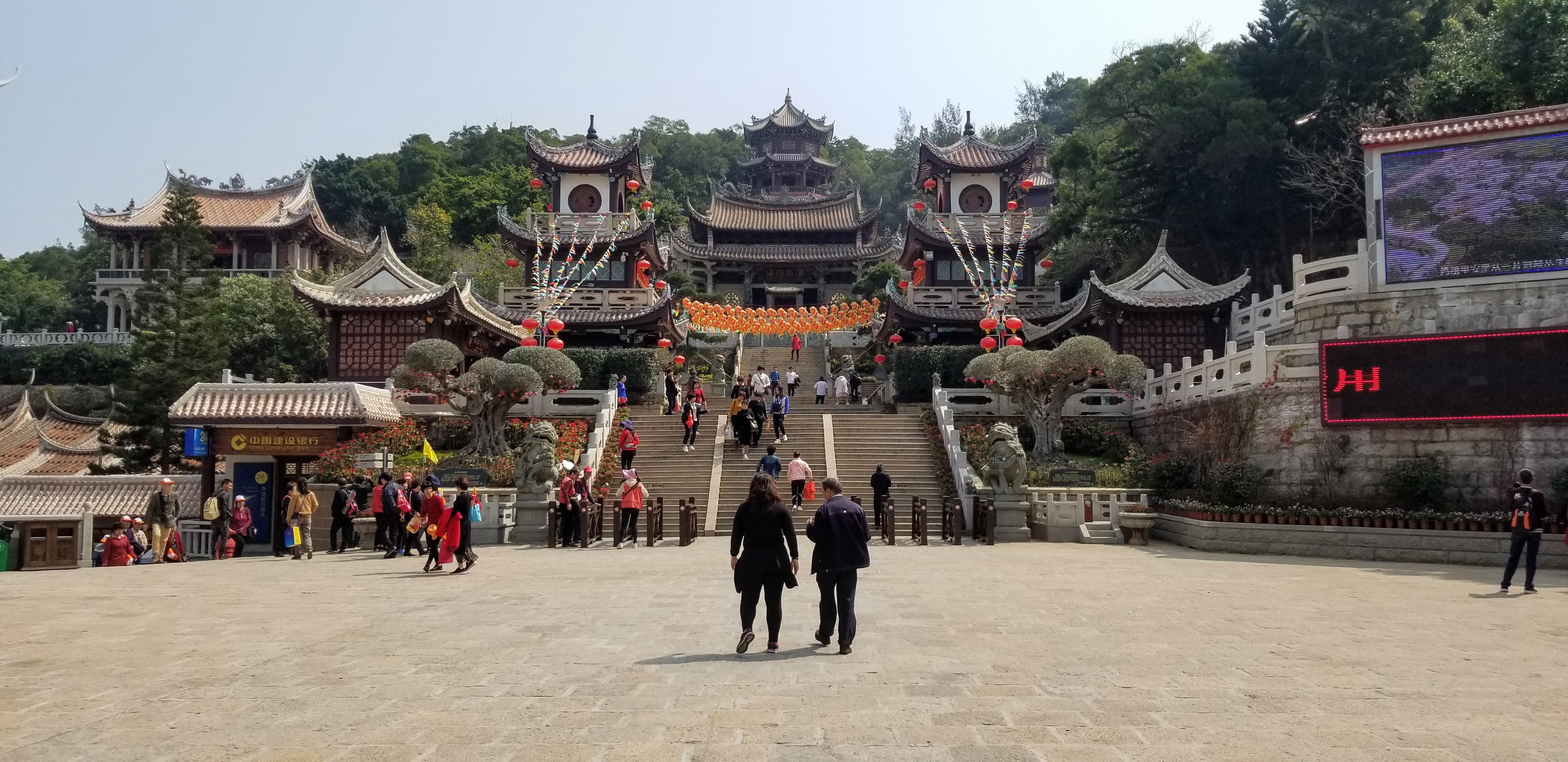 Visitors walking toward temple buildings and lanterns on a hillside