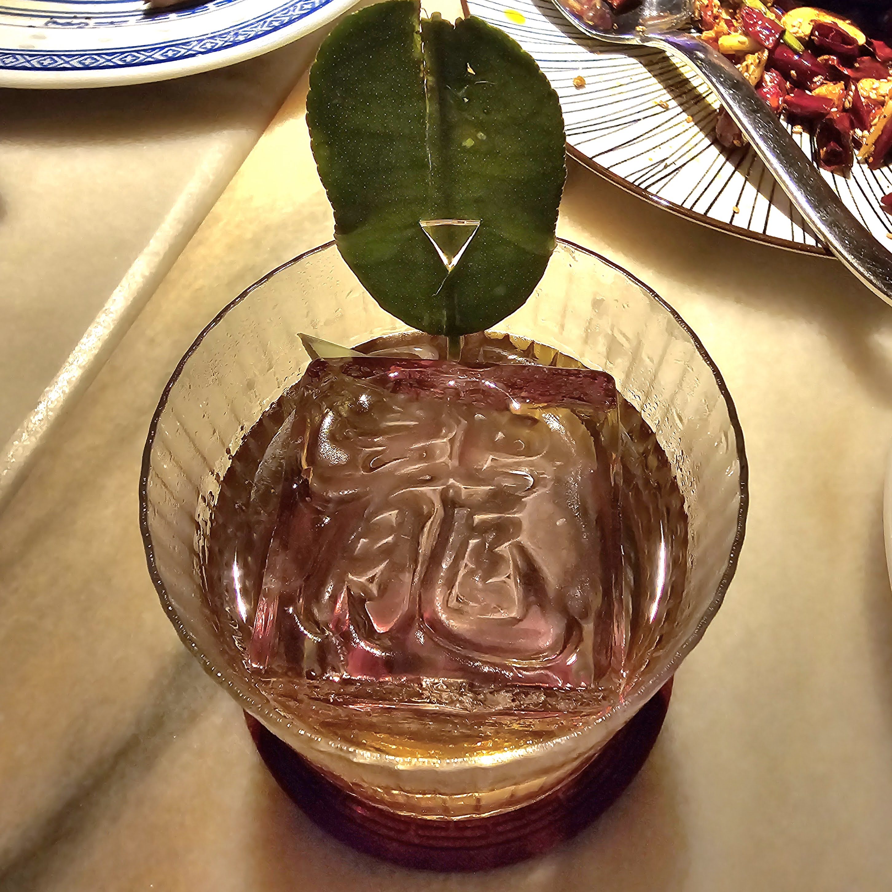 Cocktail with a large stamped ice cube and a green leaf garnish