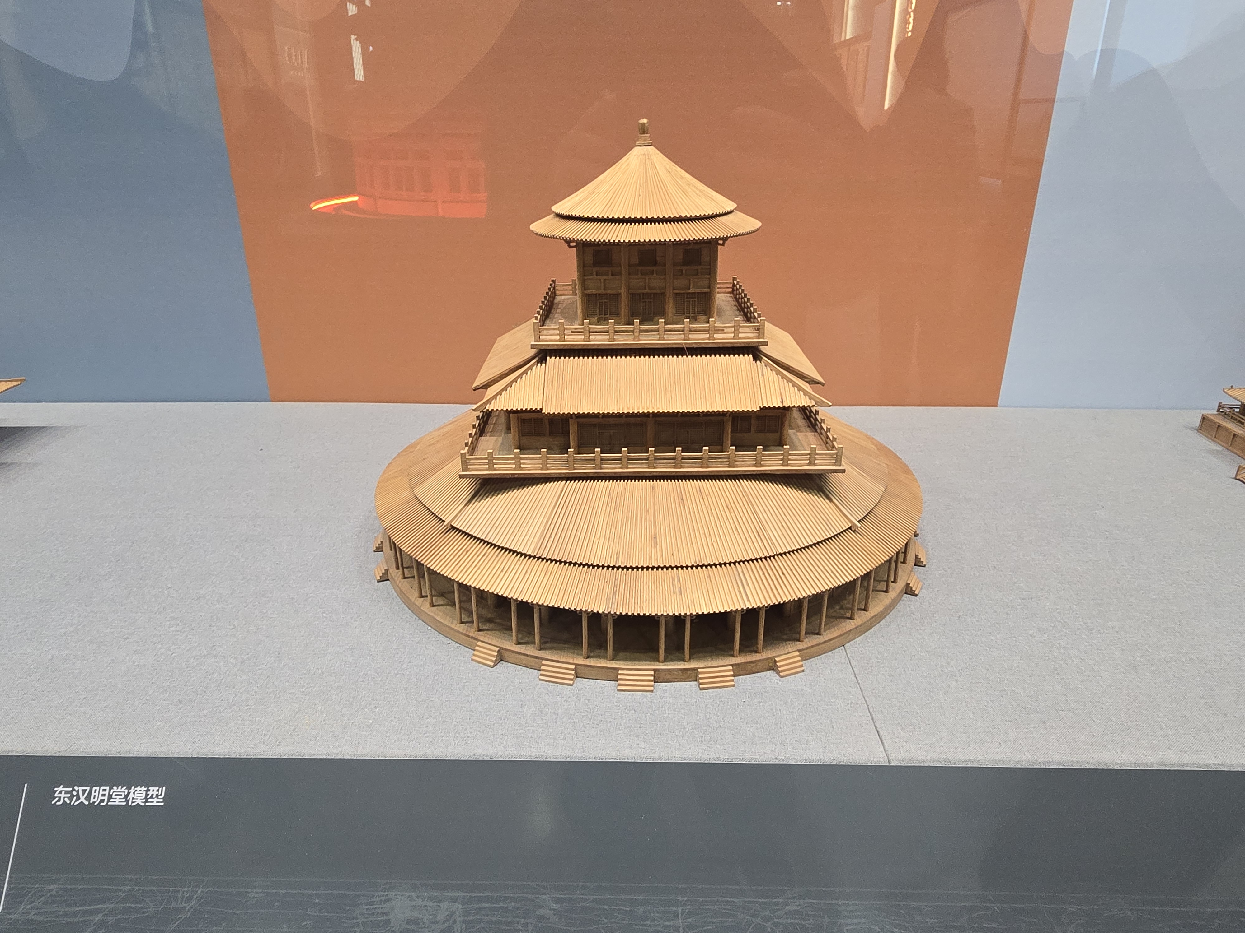 A circular timber model capped by a shallow roof.