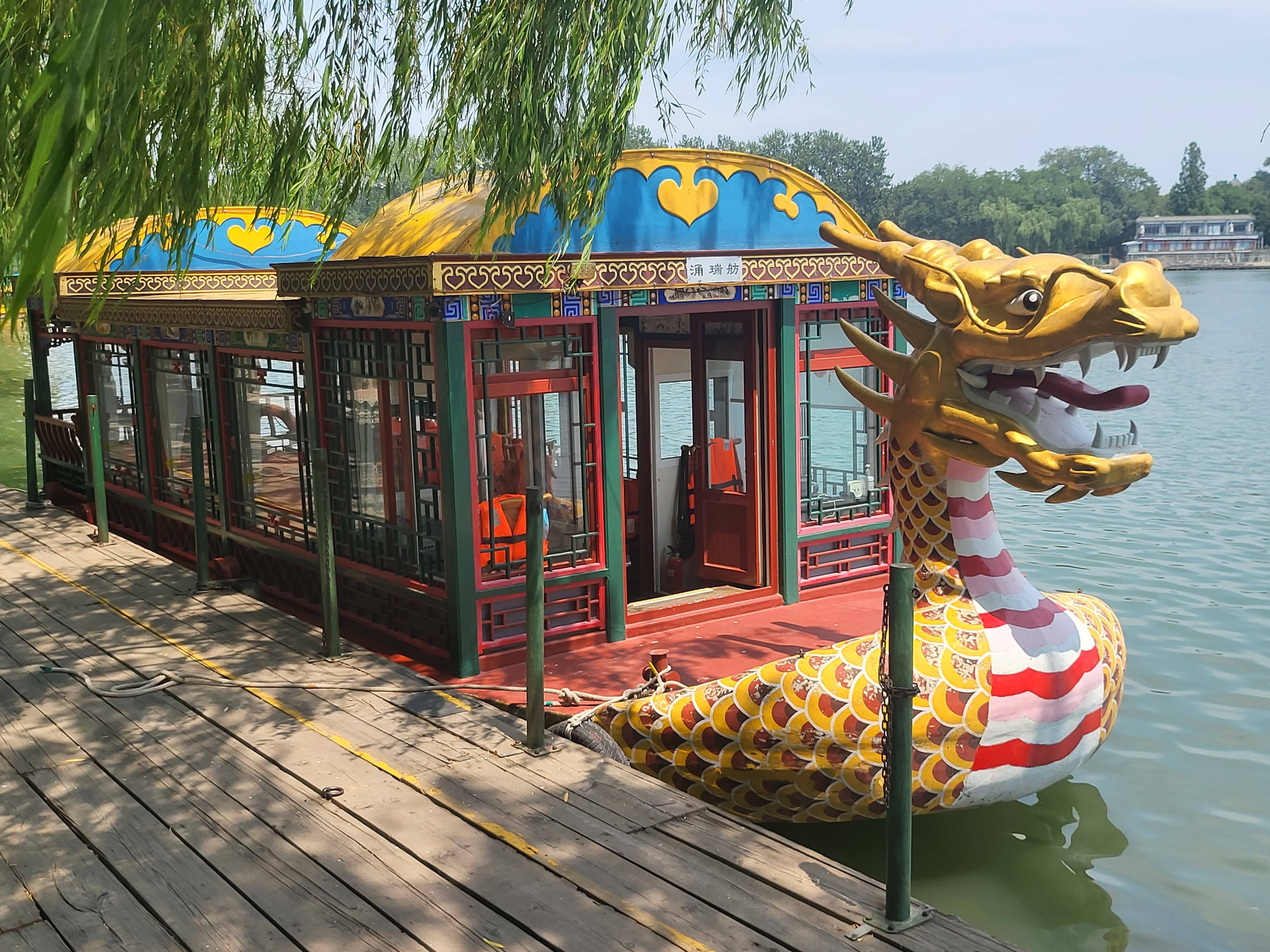 A covered dragon boat moored beside the willow-lined shore.