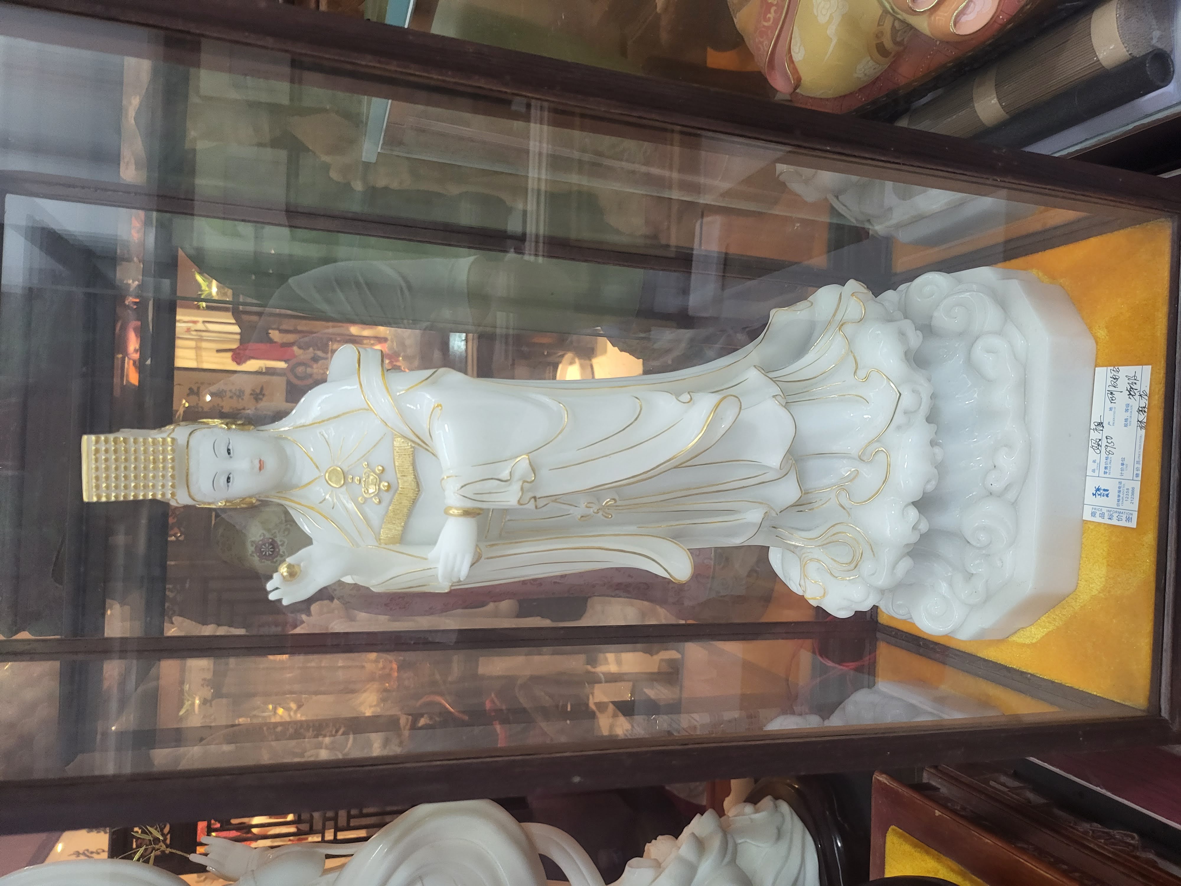 A pale standing figure displayed in a glass cabinet.
