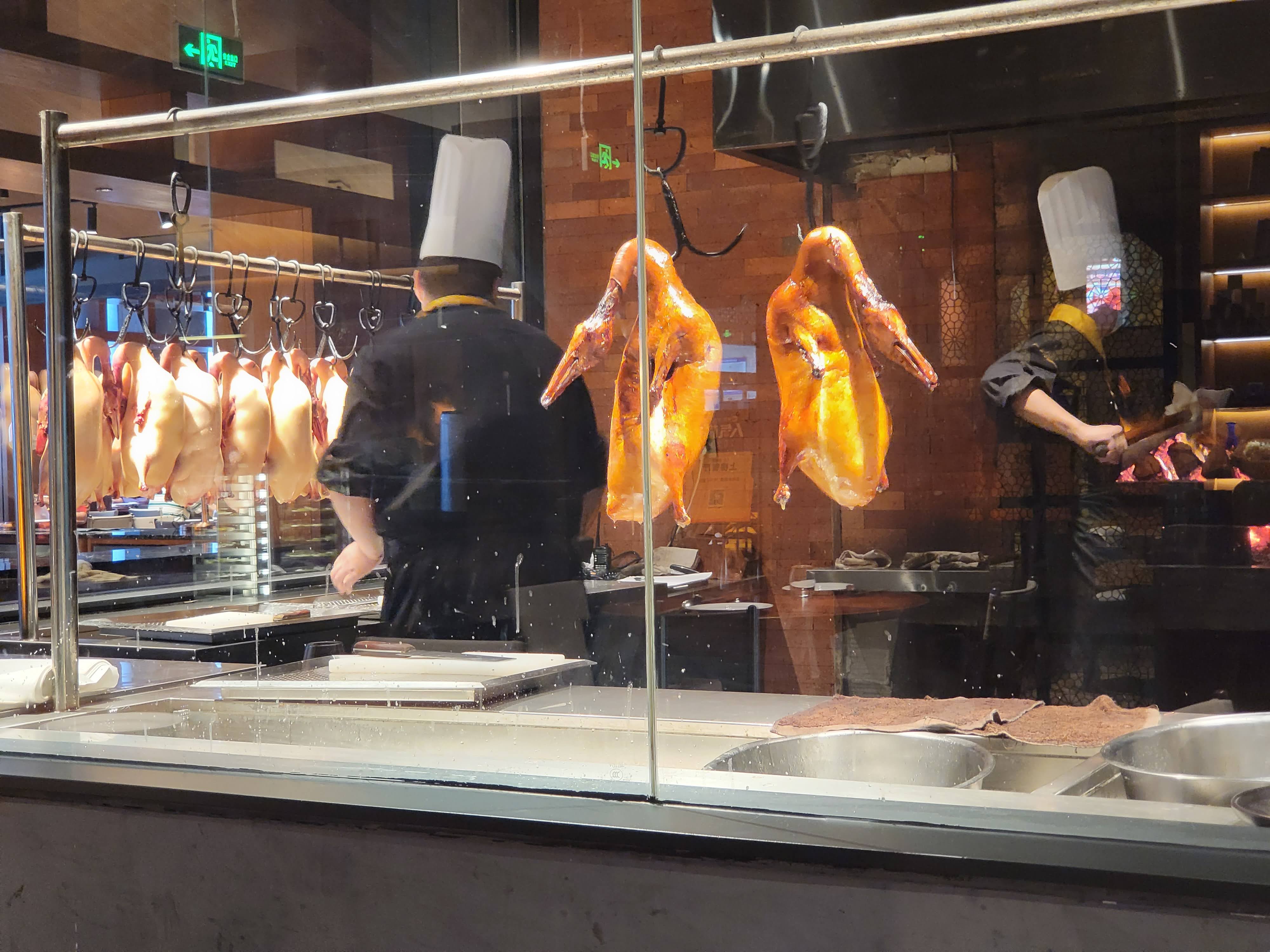 Roast ducks hang beside the open preparation area.